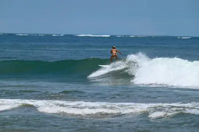 a woman riding a wave on a surfboard in the ocean at Beautiful beachfront 2BR condo, with full kitchen in Tamarindo