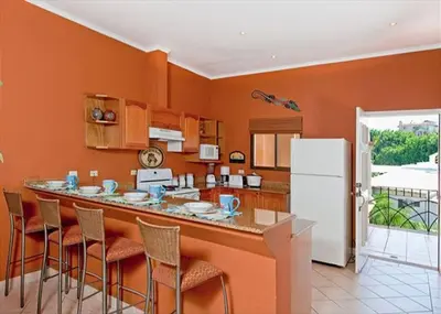 a kitchen with orange walls and a bar with stools at Beach Facing, large pool & guard in the town in Tamarindo