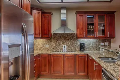 a kitchen with wooden cabinets and a stainless steel refrigerator at Beachfront, Sunset, & Ocean Views with Elevator in Tamarindo