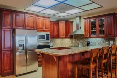 a kitchen with wooden cabinets and a stainless steel refrigerator at Beachfront, Sunset, & Ocean Views with Elevator in Tamarindo