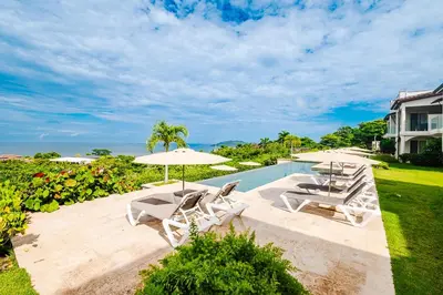a pool with chairs and umbrellas next to a house at Brand New Ocean View Condo overlooking Tamarindo in Tamarindo