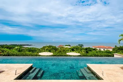 a swimming pool with umbrellas and the ocean at Brand New Ocean View Condo overlooking Tamarindo in Tamarindo