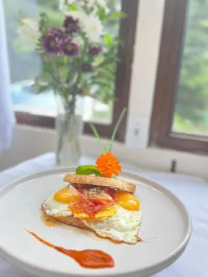 a plate with an egg sandwich on a table with a vase of flowers at Freddy`s Place B&B in Monteverde Costa Rica