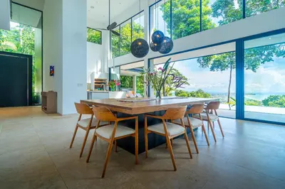 a dining room with a table and chairs and large windows at Casa Colibri - by Pura Villas in Uvita