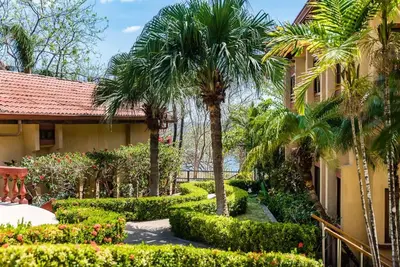 a garden with palm trees and a building at Light & Breezy Beach Side Condo! in Tamarindo