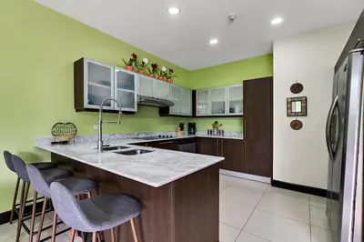 a kitchen with green walls and a counter with stools at Pura vida charm, canopy views, block from beach in Tamarindo
