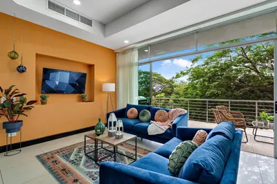 a living room with blue furniture and a large window at Pura vida charm, canopy views, block from beach in Tamarindo