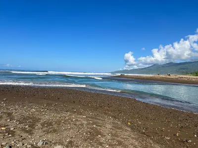 a beach with rocks and water and mountains in the background at Cabañas MOHES ballena in Uvita