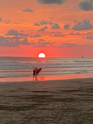 two people standing on the beach with a surfboard at sunset at Cabañas MOHES ballena in Uvita