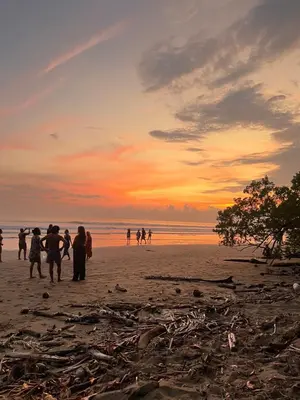 a group of people walking on a beach at sunset at Cabañas MOHES ballena in Uvita