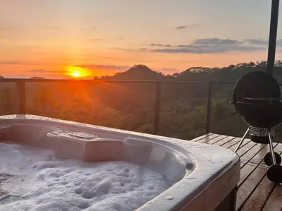 a hot tub on a deck with the sunset in the background at GoldenView+ Aire acondicionado+Jacuzzi (a 15 km de Monteverde) in Monteverde Costa Rica