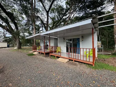 a small white building with a porch next to trees at Macaw Paradise in Jacó