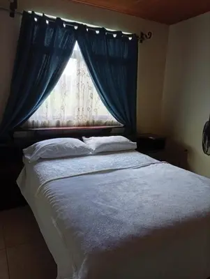 a bedroom with a bed with a window with blue curtains at Casa morfo in Bijagua
