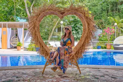 a woman sitting on a wicker chair in front of a pool at ECOTICA Boutique Hotel & Spa in Manuel Antonio