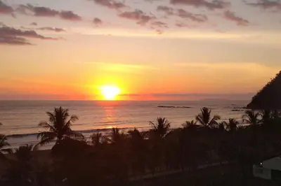 a sunset over the ocean with palm trees on the beach at Rooftop balcony oceanfront PH condo with King beds in Jacó