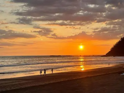 a group of people walking on the beach at sunset at Rooftop balcony oceanfront PH condo with King beds in Jacó
