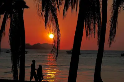 a group of people walking on the beach at sunset at Hotel El Velero in Playa Hermosa