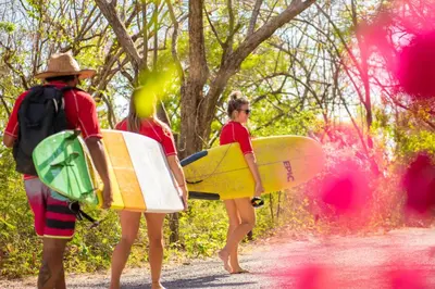 three people walking down a dirt road holding surfboards at Playa Grande Surf Camp in Playa Grande
