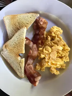 a white plate with scrambled eggs and bacon and toast at Manatus Hotel in Tortuguero