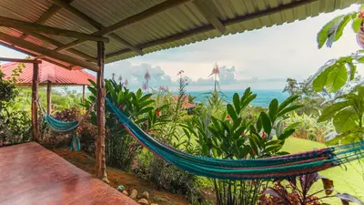 a hammock on a porch with a view of the ocean at Cabañas Caeli, La Perezosa, La Fortuna Rainforest Glass Cabin w Amazing Views in Fortuna