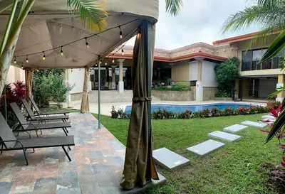 a patio with chairs and an umbrella and a pool at Luxury House near to Juan Sant. Airport, Alajuela. in Alajuela City