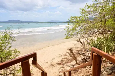 a sandy beach with a wooden railing and the ocean at Casa Corona Del Mar Tamarindo in Tamarindo