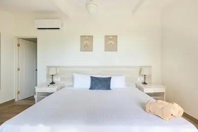 a white bedroom with a large white bed with blue pillows at Perla de la Playa Beachfront Hotel in Tamarindo