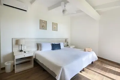 a white bedroom with a large white bed and a nightstand at Perla de la Playa Beachfront Hotel in Tamarindo
