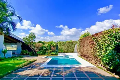 a swimming pool in a garden with a hedge at Hermosa Habitación privada en la Sabana, San Jose in San José