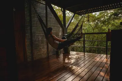 a man is sitting in a hammock on a porch at NATURAVE - Into the woods - Mountain cabins in Monteverde Costa Rica