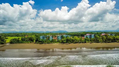 a view of a beach with buildings in the background at Beachfront Condo - your Oasis with pool and Wi-Fi in Bejuco