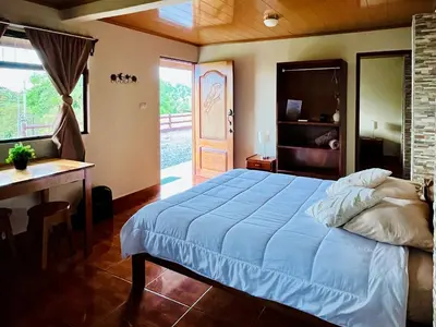 a bedroom with a bed and a desk and a door at Los Tucanes Lodging in El Castillo de La Fortuna