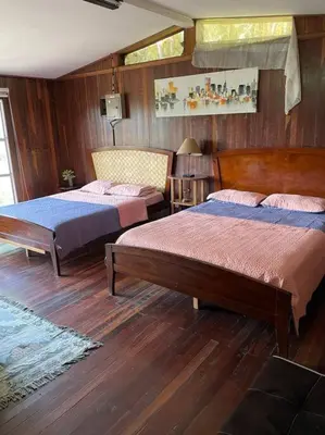 two beds in a bedroom with wooden walls and wood floors at Rainforest Cabin in Escazu in Escazu