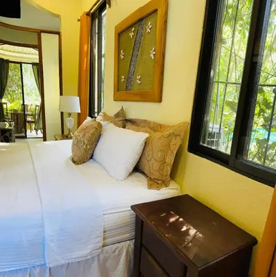 a bedroom with a bed with white sheets and windows at Enchanted sonido de la selva in Quepos