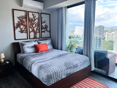 a bedroom with a bed and a large window at CityScape Properties 20th floor Studio 24-7 Concierge Amenities in San José
