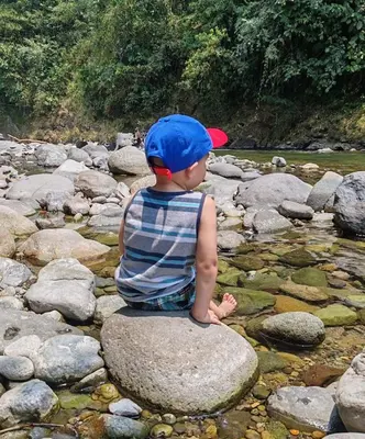 a young boy sitting on a rock in the water at Cabaña Dream House in Pejibaye