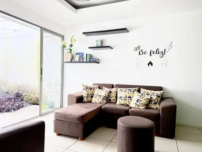 a living room with a brown couch and a window at Casa Matiza, 7 min SJO airport, free parking, AC in Santiago Este
