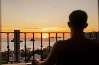 a person looking out a window at the sunset at El Prado: New 2br Condo in Las Catalinas in Playa Danta