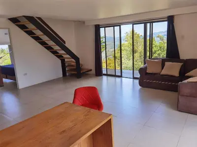a living room with a couch and a red chair at Casa Roble Cabaña romántica en la montaña de Costa Rica in San Cristóbal Sur