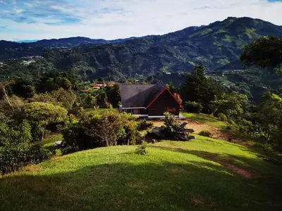 a red barn on a hill with mountains in the background at Casa Roble Cabaña romántica en la montaña de Costa Rica in San Cristóbal Sur
