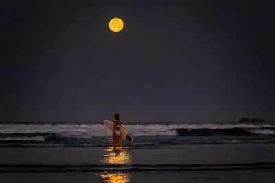 a woman walking on the beach at night with a surfboard at Direct Beach & Pool Access l 247 Security in Jacó