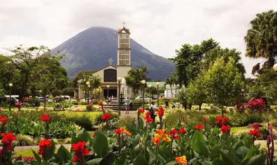 a church with a mountain in the background with flowers at Casa Paraíso - La Fortuna in Fortuna
