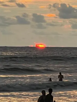 a group of people standing on the beach watching the sunset at Cabañas MOHE’S Uvita in Uvita