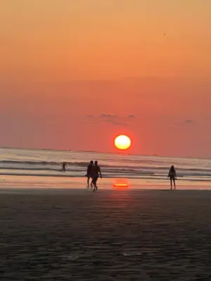 a group of people walking on the beach at sunset at Cabañas MOHE’S Uvita in Uvita