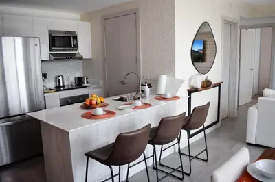 a kitchen with a large white island with bar chairs at Apartamento con piscina y espacio de trabajo in San José