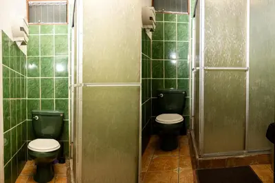 a bathroom with two toilets and green tiled walls at Manuel Antonio Hostel in Manuel Antonio