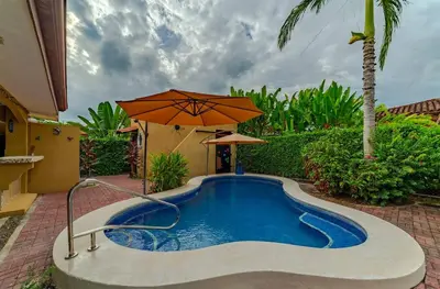 a swimming pool with an umbrella next to a house at Villa Felicidad by Vacation Pura Vida in Esterillos