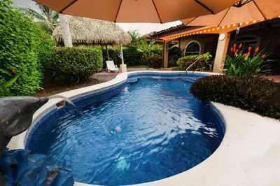 a swimming pool with an umbrella next to a house at Villa Felicidad by Vacation Pura Vida in Esterillos