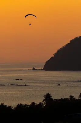 a paraglider flying over the ocean at sunset at Modern 2 Bed 2 Bath l Strong Wifi Carport in Jacó