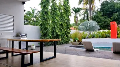 a patio with a table and a bench and a pool at Casa Arribada- Bright 4Br House 5-min walk to Beach, Pool, BBQ in Playa Flamingo